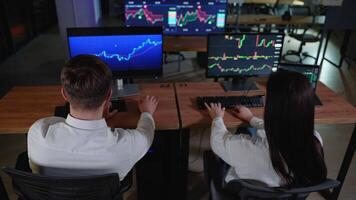 Rear view of creative team of traders are having a conversation in a dark office with display screens. Analyzing data, graphs and reports for investment purposes video