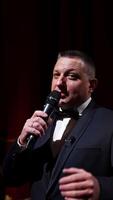 Presenter with microphone announces performance before auditorium from stage. Theater curtains background. Vertical video