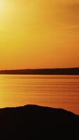 Amazing view of a golden sunset path over water surface and a biker. Silhouette of a male biker in helmet rides up to the river during the setting sun. Vertical video