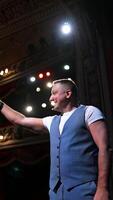 Man in front of theater hall put hand to ear. Actor is standing on stage and talking with public during the performance. Classic theater interior. Vertical video