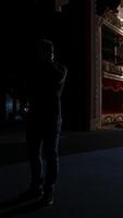 Theater actor has rehearsal before performance. Dark light behind scene. Man in formal clothes with handfree microphone. Classic theater concept. Vertical video