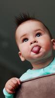 Funny boy with sticking out hair standing on a chair. Kid holding both hands on a chair back and turning his head away from camera. Low angle view. Blurred backdrop. Vertical video