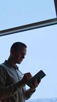 Focused man standing in office with notebook in hands. Businessman taking notes near the big window. Cityscape at backdrop. Vertical video