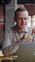 Middle aged man sitting at the computer and smiling broadly. Pleasant working atmosphere in a light office. Vertical video