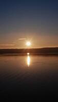 River at sunset. Setting sun reflects on the water surface in the evening. Beautiful view of the lake with setting sun on the evening sky. Vertical video