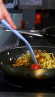 Cooking and stirring the spaghetti with red tomatoes and mushrooms in the frying pan. from a side. Vertical video