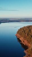 Calm lake in the evening. Boat moving on the river at sunset. Beautiful nature background. Trees reflected in water. Aerial view. Vertical video