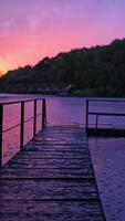 vide en bois pont plus de le rivière pendant le pluie à le coucher du soleil. le passerelle dans le Lac sur le Contexte de des arbres dans le soir. verticale video