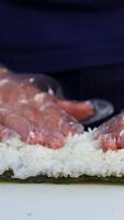 Chef in gloves is preparing sushi. Sushi are made of rice, nori seaweed, cucumber, cream cheese. Appetizing and nutritious food concept. Vertical video