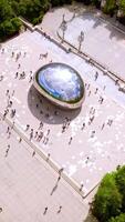 Iconic Cloud Gate surrounded by numerous tourists visiting the site. Top view on the blue cloudy sky reflecting in the big shining Bean. Vertical video