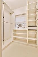 A white walk in closet with shelves and a window photo