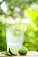 Glass of cold water with fresh lime slices, healthy drink of lime with lime slices placed on wooden table and natural background photo