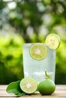 Glass of cold water with fresh lime slices, healthy drink of lime with lime slices placed on wooden table and natural background photo
