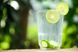 Glass of cold water with fresh lime slices, healthy drink of lime with lime slices placed on wooden table and natural background photo