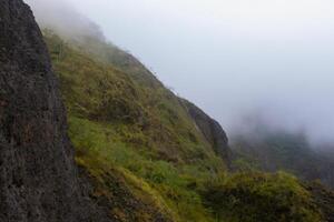 The slopes of Mount Kelud with green bushes and trees, and thick fog hanging above it. One of active volcanoes in East Java, Indonesia. photo