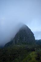 The Sumbing Cliffs of Mount Kelud partly covered in thick fog, a ridge consisting of dark gray andesite rocks in a beautiful cone shape with a slope of almost 90 degrees. photo