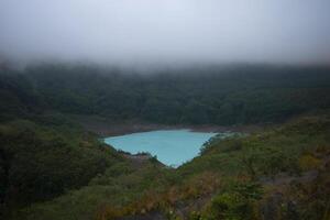 Beautiful view of the crater of Mount Kelud when it is inactive with turquoise lake water and thick fog above it. photo