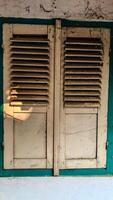 A pair of old, wooden window shutters painted in light beige with a teal frame. photo