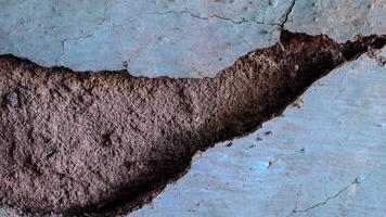 cracked and weathered wall surface. The paint is peeling and the concrete is exposed, creating a textured and distressed look photo