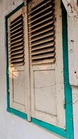 A pair of old, wooden window shutters painted in light beige with a teal frame. photo