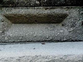 weathered concrete surface, showcasing the rough texture, cracks, and shadows created by its uneven surface. photo