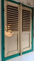 A pair of old, wooden window shutters painted in light beige with a teal frame. photo