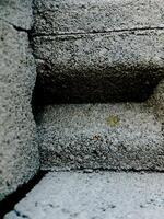 weathered concrete surface, showcasing the rough texture, cracks, and shadows created by its uneven surface. photo
