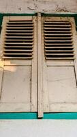A pair of old, wooden window shutters painted in light beige with a teal frame. photo