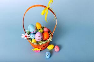 Top view of wicker basket filled with decorative multi colored eggs on a light blue background photo