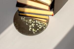 three old books lie with white gypsophila flowers and a round mirror on the table in the sunlight photo
