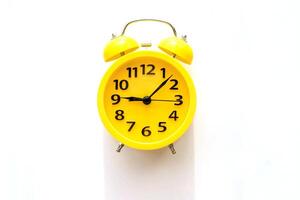 A yellow alarm clock with a black dial lies on a white table, top view photo