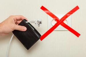 A mans hand holds a wallet with a white cord hanging from it with a plug near an electrical outlet photo