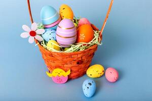Close up of wicker basket filled with decorative multi colored eggs on a light blue background photo
