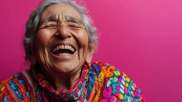 Close-up of a joyful elderly woman laughing heartily, wearing a colorful garment, expressing pure happiness and warmth against a bright pink background. photo