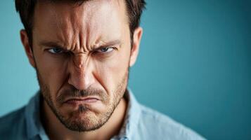 Close-up portrait of an angry man with a furrowed brow and intense expression, glaring directly at the camera against a plain background. photo