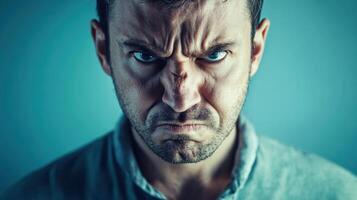 Close-up portrait of an angry man with a furrowed brow and intense expression, glaring directly at the camera against a plain background. photo