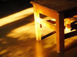 A wooden table is sitting in the sun, casting a shadow on the floor. The sunlight is warm and inviting, creating a cozy atmosphere photo