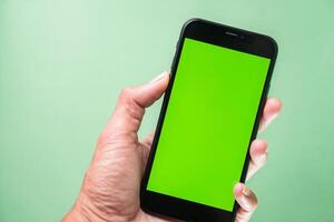 Hand holding smartphone with green screen on green background photo