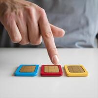 Hand pointing at three colorful SIM cards on a white surface For Social Media Post Size photo