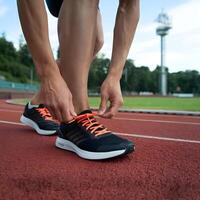 Close up of lower body tying shoelaces on red running track, greenery background For Social Media Post Size photo