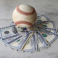 Baseball atop fanned US dollar bills on a light surface For Social Media Post Size photo