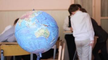 The globe stands on a desk against the background of schoolchildren who are communicating with each other. Minsk, Belarus - May 7, 2024 video