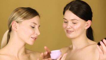 Two young women with perfect skin are holding a jar of moisturizing cream, on a yellow background video
