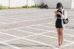 A woman in a hat and shorts is looking at her phone photo