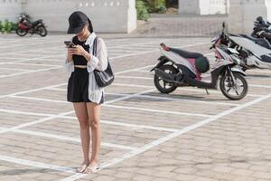 A woman standing in a parking lot with a cell phone photo