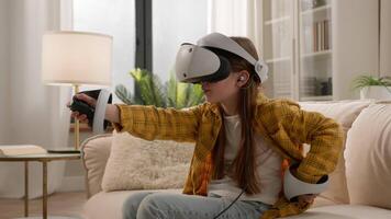 Curious Caucasian child girl little kid wear virtual reality headset vr gear wireless device. Schoolgirl daughter use controllers playing 3d game in metaverse cyberspace world online home couch video