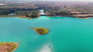 Turquoise lake with a dam holding back the water. A small island is in the middle of the lake. The camera is slowly panning from left to right video