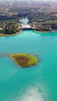 Turquoise lake with a dam holding back the water. A small island is in the middle of the lake. The camera is slowly panning from left to right video