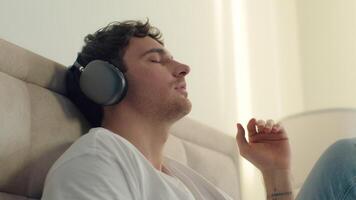Caucasian man male guy listening music headphones closed eyes enjoyment relaxing sing song gadget technology playlist radio bedroom home satisfaction earphones audio device wireless connection sound video