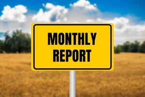 Monthly report message written on yellow metal sign on blurry wheat field background. Conceptual monthly report symbol. Copy space. photo